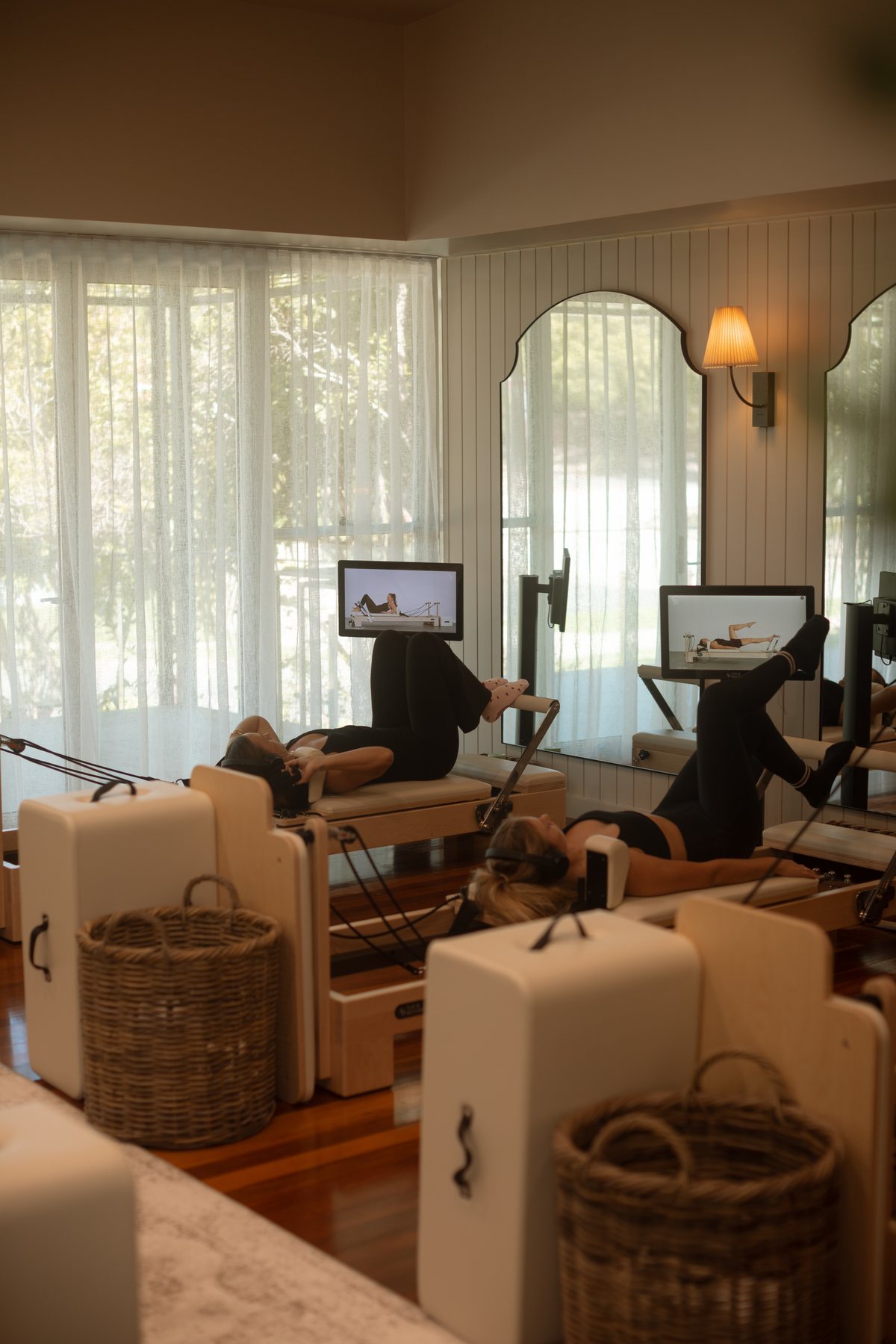 Two members working through a reformer session beside the studio windows